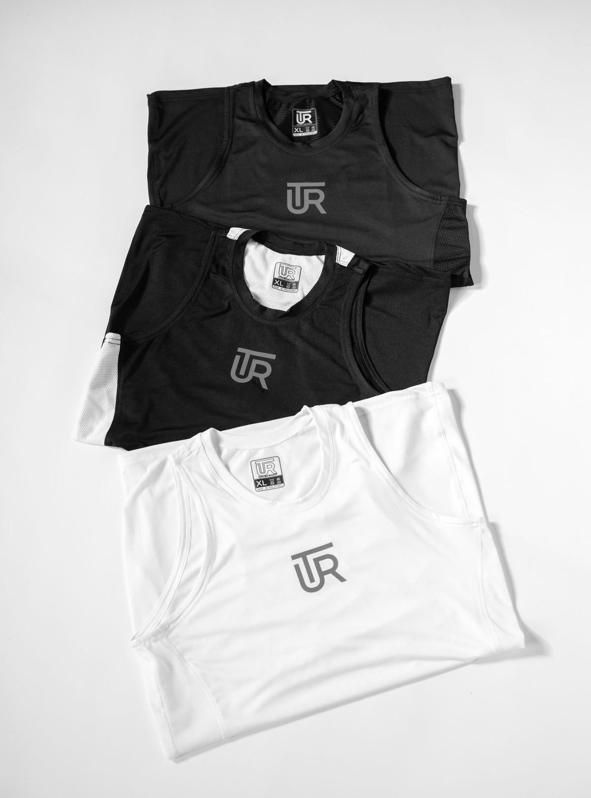 UTR Classic Sport sleeveless compression jerseys in Black, Monochrome and White with gray UTR logo, flat lay